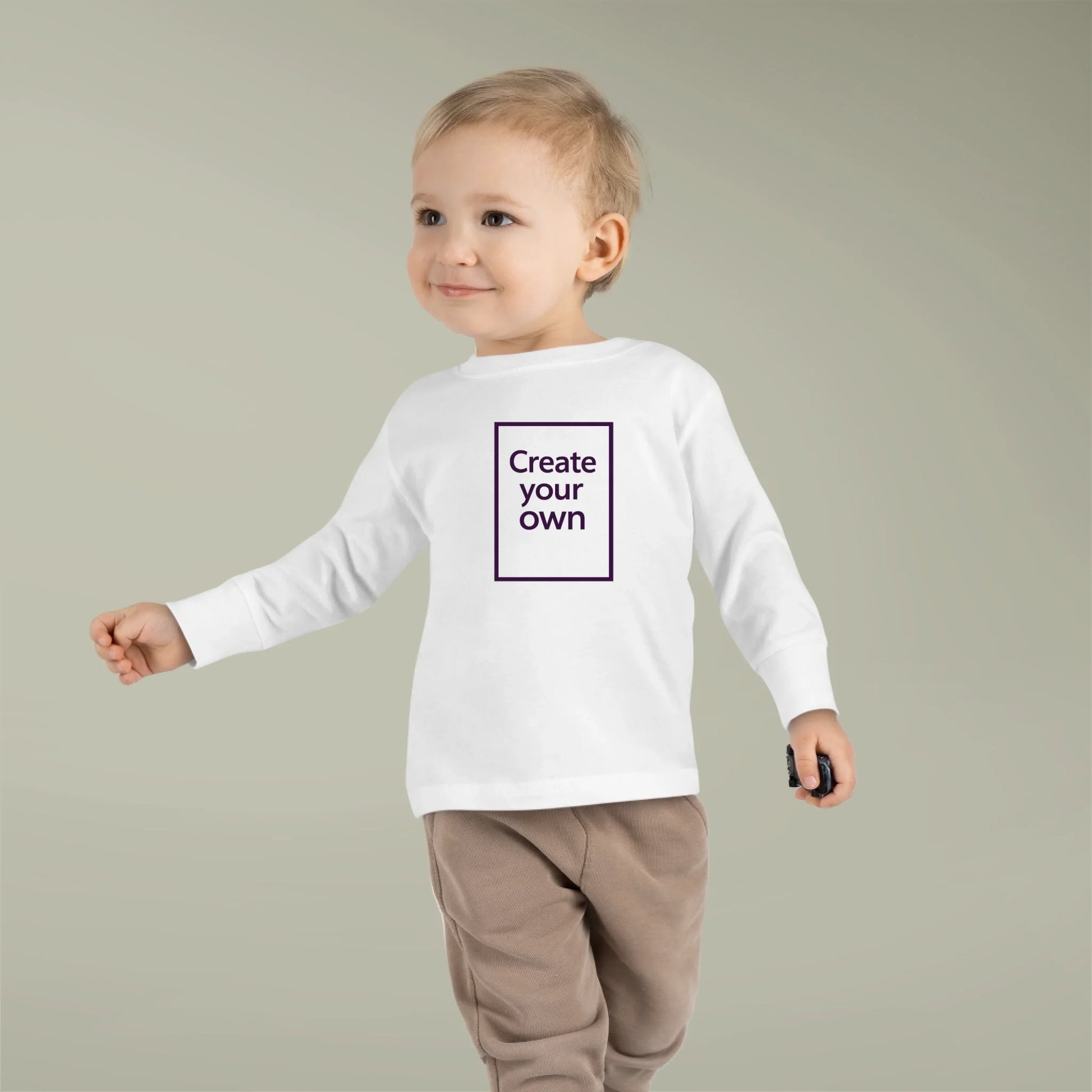 Child wearing a white long-sleeve shirt with 'Create your own' text on a plain background